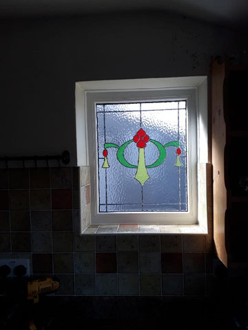 A stained glass window with a floral design in a sunlit kitchen