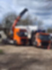 Two bright orange trucks with cranes lift a large, covered load in a construction site