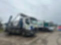 Two skip hire trucks are parked in a yard, one with a large open skip attached