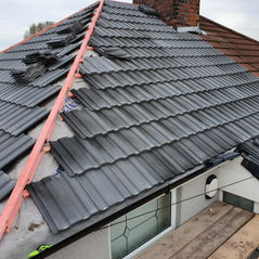 Partially completed roof under construction, with black tiles and visible red wooden supports