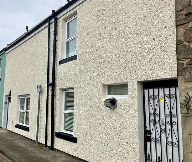 A white stucco house with black trim features three windows and a decorative metal gate