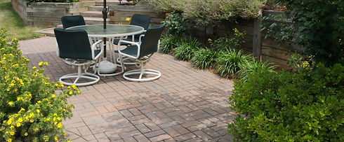 Circular glass garden table with four black chairs situated on a light stone paved patio area
