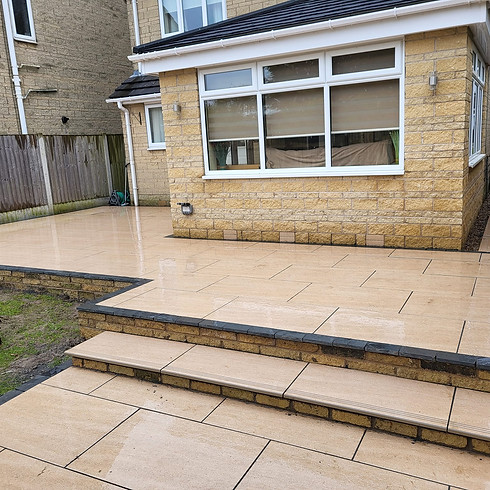 Wet patio with beige tiles in an outdoor space with a visible brick house with large windows