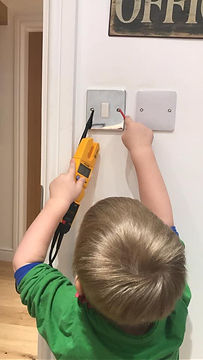 A young child uses a multimeter on a light switch