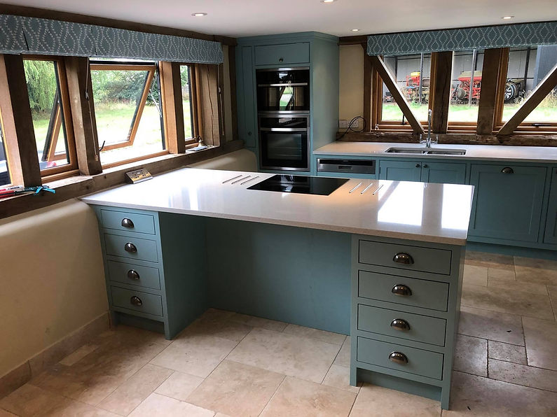 Spacious kitchen with a light blue island featuring a black stovetop. Surrounded by wood-framed windows and cabinets