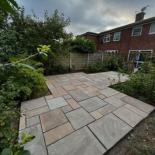 A newly laid stone patio in a back garden, bordered by lush greenery