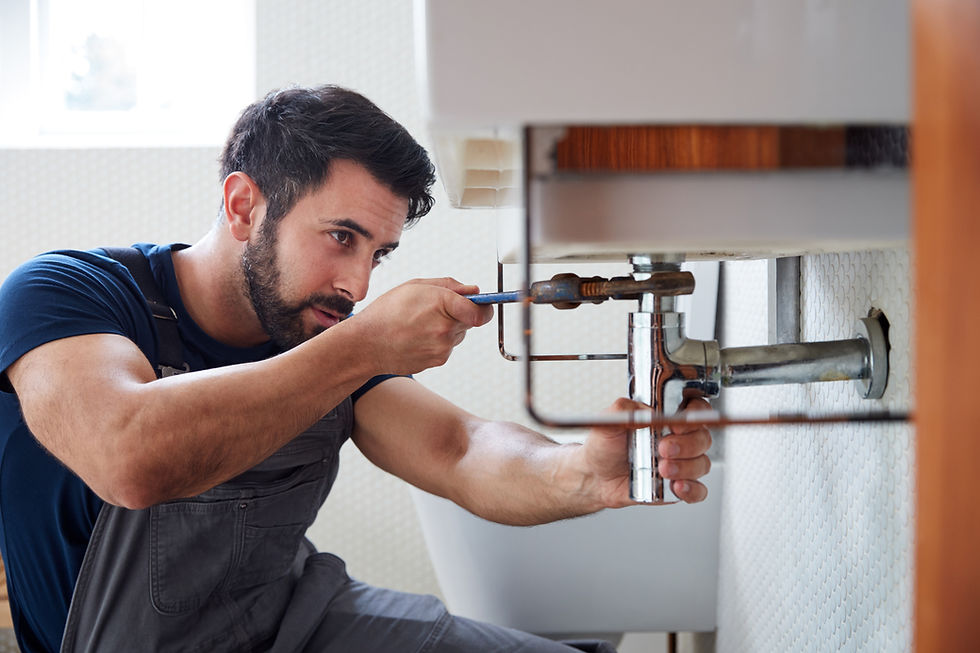 A plumber repairing a pipe under the sink using a wrench