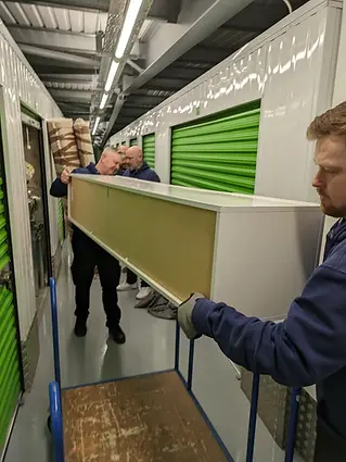 Men moving a large piece of furniture onto a cart in a storage facility