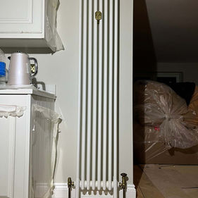 A modern white radiator stands against a light wall in a kitchen