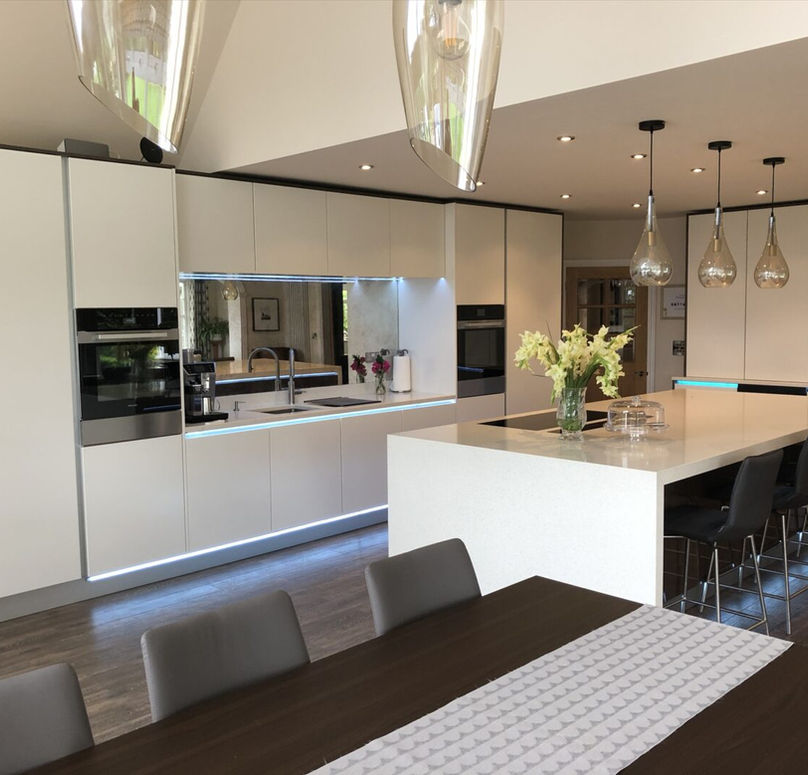 Modern kitchen with sleek white cabinetry, a large island, and stylish pendant lights, featuring fresh flowers and dark wood accents