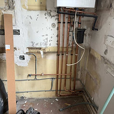 A room showing exposed walls, copper and plastic plumbing pipes, a gas boiler, and construction materials