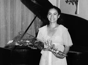 A person stands in front of a grand piano, holding a bouquet