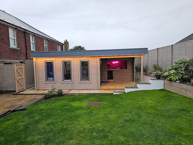A modern garden shed with pink interior lighting and a covered deck