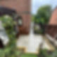 A paved garden path with an archway covered in leafy vines leads between two brick buildings
