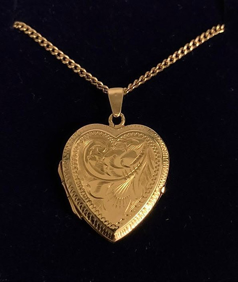 A solid 9ct yellow gold curb-link chain necklace supporting a beautifully hand-engraved heart locket featuring traditional scrollwork patterns against a dark backdrop. 