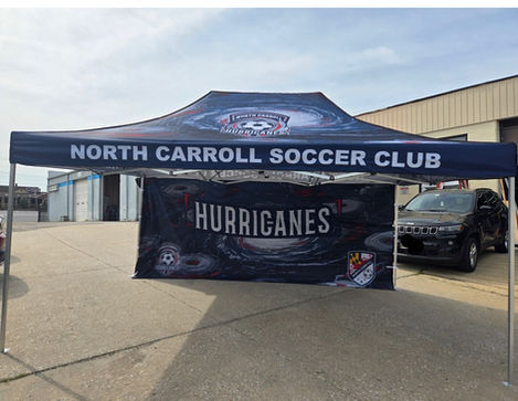 A large black pop-up canopy tent with white and blue graphics for the "NORTH CARROLL SOCCER CLUB HURRICANES" set up outdoors on grass.
