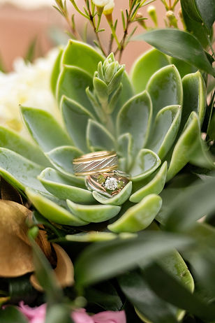 Gold and Silver, Diamond and Peridot Wedding rings and bands sit on a succulent bouquet, ready for the wedding and marriage.