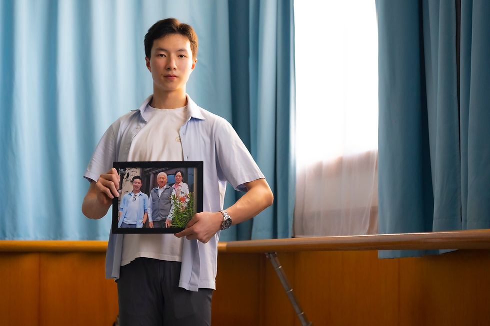 A person holds a framed photo of three people, standing in a room with blue curtains and wooden paneling. The scene is calm and reflective.