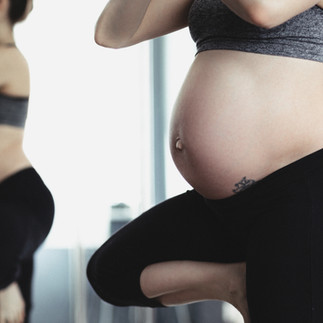 Detalle de vientre de mujer embarazada en ropa deportiva durante clase de yoga.