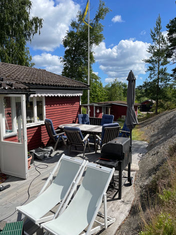 Altan med utemöbler och grill vid rött fritidshus i Uttervik före ombyggnation.