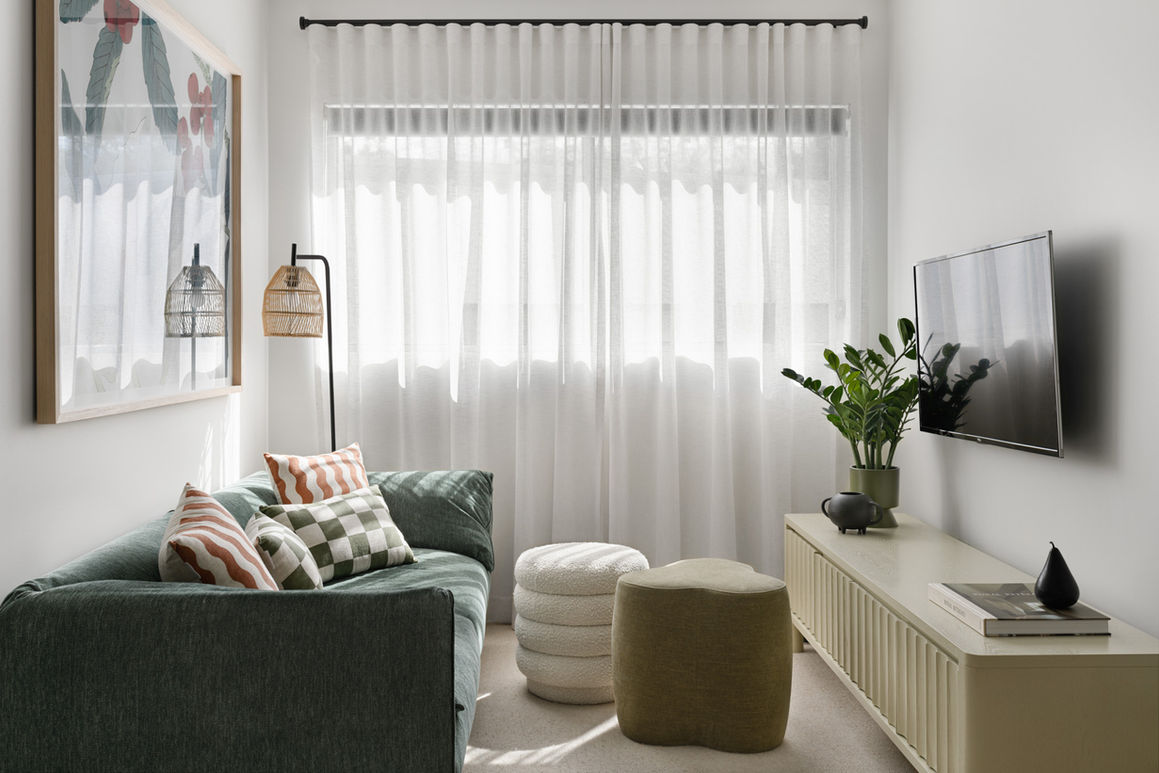 Modern living room with a green velvet couch, striped and checkered cushions, and natural light streaming through sheer white curtains, designed by Porch Light Interiors, Brisbane interior designer.