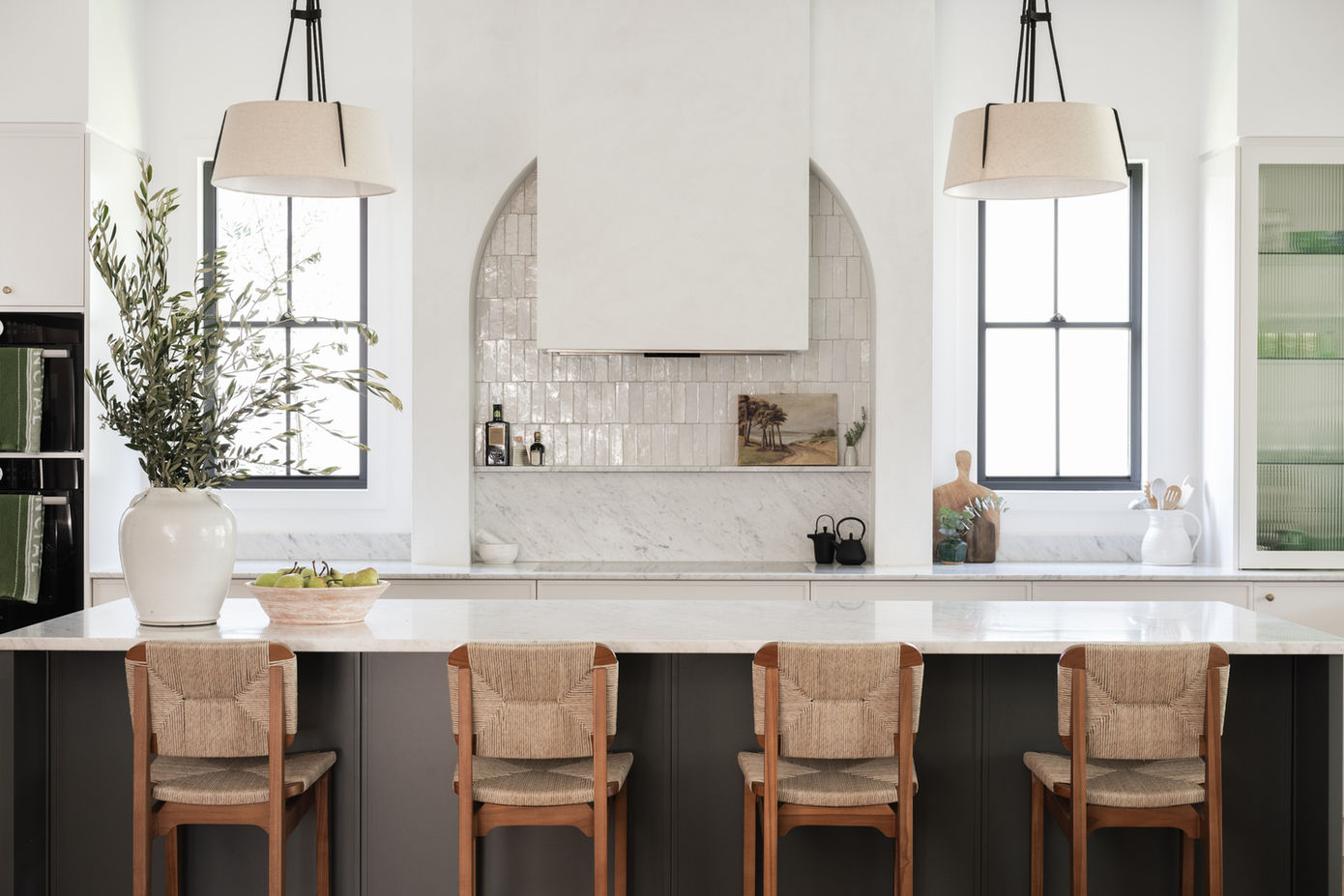 Bright kitchen with a large white marble island, arched tiled backsplash, and timber bar stools, designed by Porch Light Interiors, Brisbane interior designer.