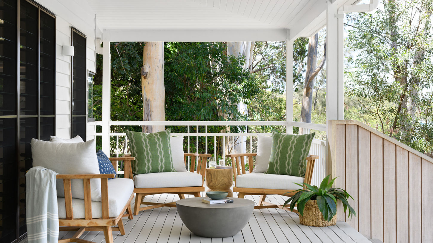 Refined Queensland verandah with timber lounge set, green-and-white cushions, and lush greenery, offering a perfect balance of comfort and style for subtropical outdoor relaxation.
