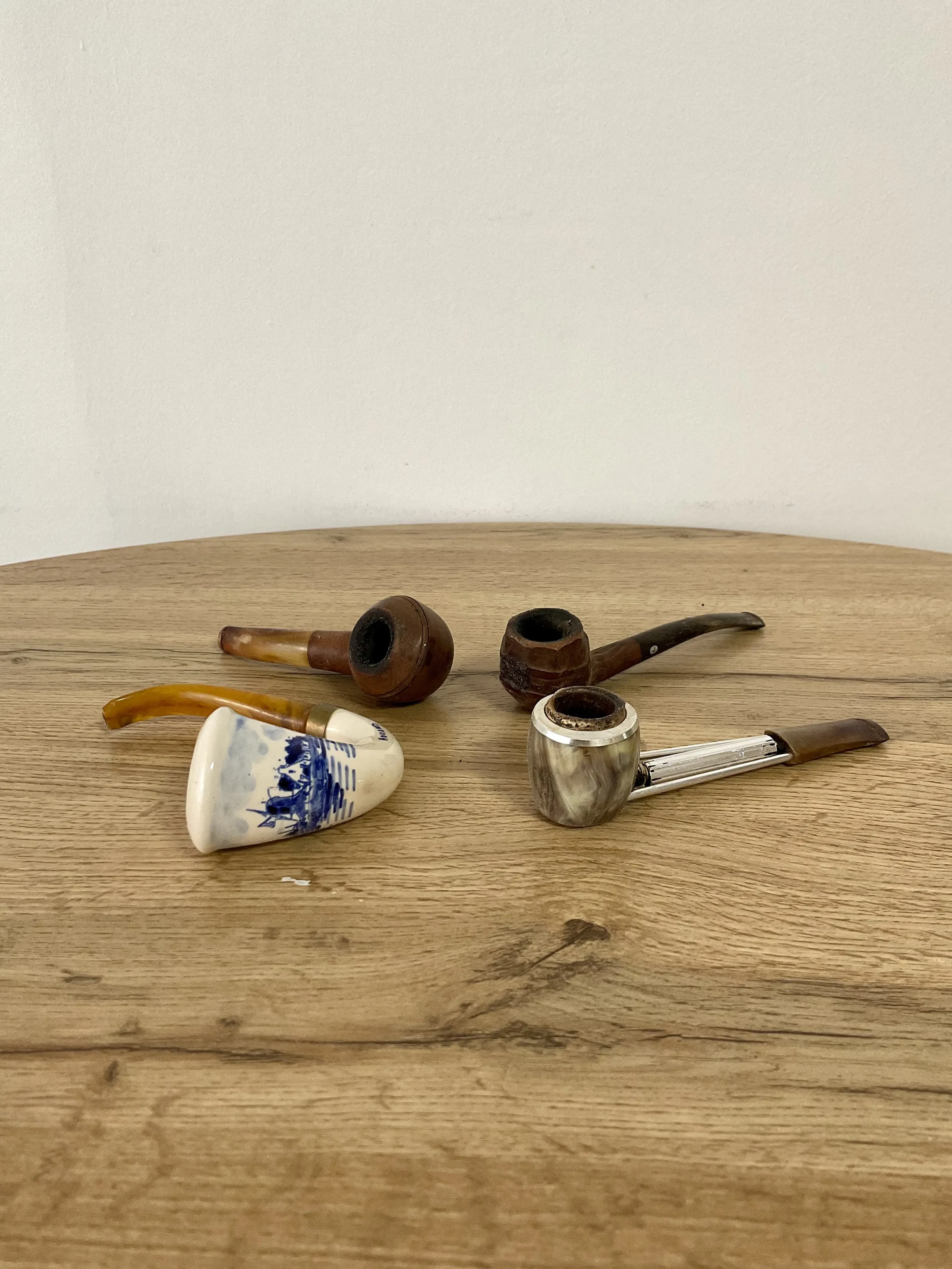 quatre pipes posé sur une table en bois, une pipe en céramique, deux pipes en bois et une pipe en métal