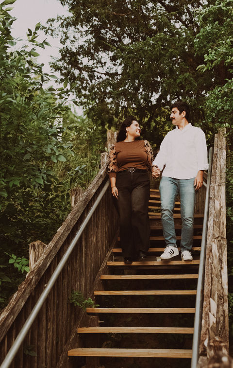 Couple holding hands walking down stairs, trees background, engagement photography, monograin.