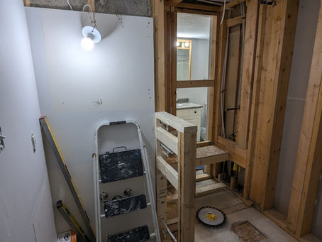 Construction site with wooden framing, ladder, light bulb, tiles, and tools. Unfinished wall and ceiling. Bright bulb illuminates room.