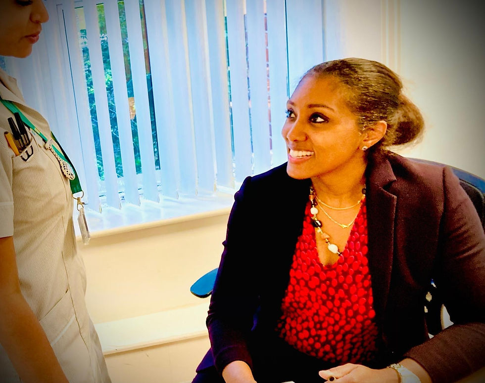 Smiling female gynaecologist in a black blazer and red blouse talks to a nurse in a bright office by vertical blinds.