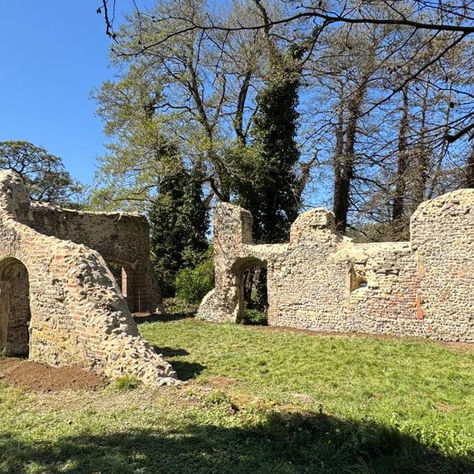 Ruins of Trowse Newton Hall with three sides of a walled structure in flint and lime work. Grass beneath and around the partial walls.