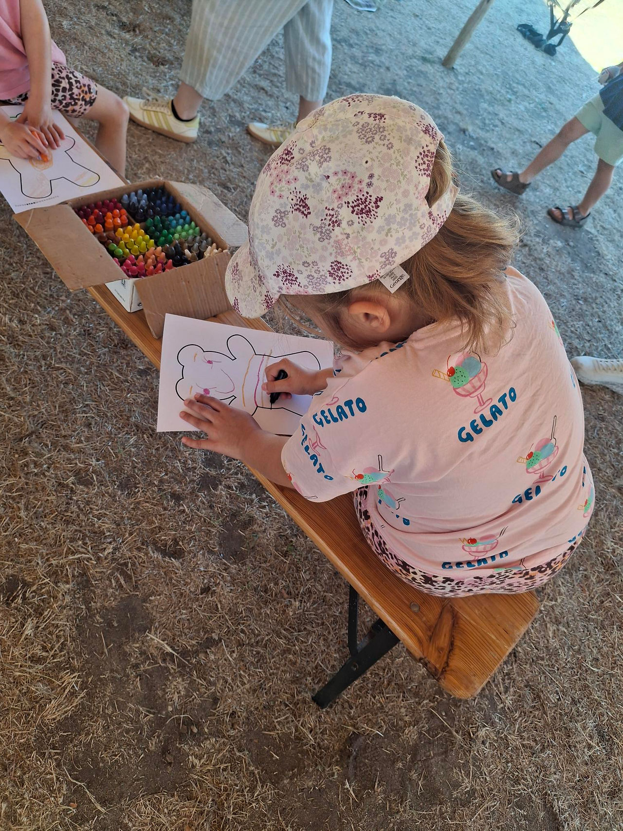 A young girl on a bench colouring in a teddy picture with a crayon