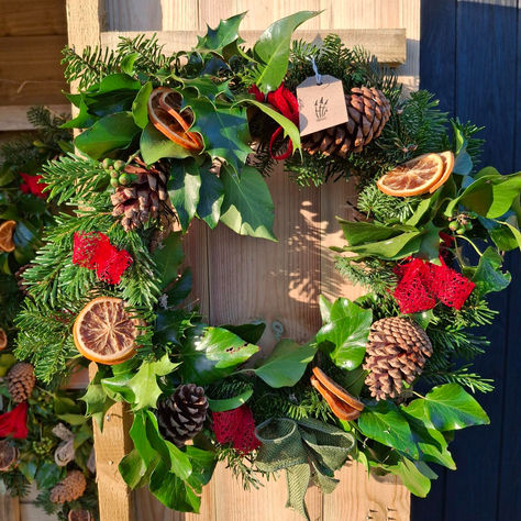 Handmade Christmas wreath with pine cones, dried orange slices, red ribbon and a green ribbon bow.