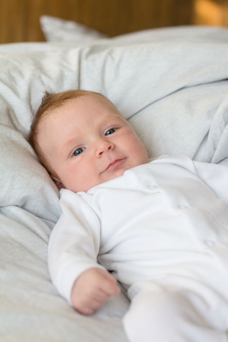 a baby in a white babygrow is laying on a bed