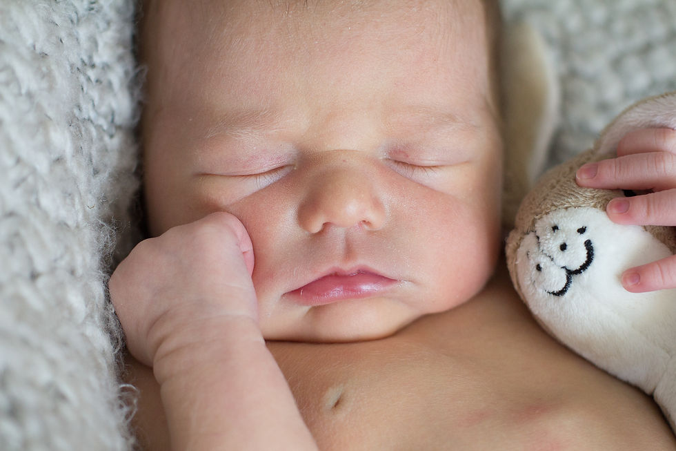 Sleeping baby holding a smiling plush toy on a soft, textured blanket. Peaceful mood with neutral and soft tones.