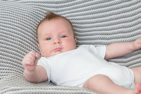 a baby in a white bodysuit is laying on a knitted blanket