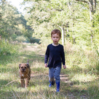 young boy walks through long grass with dog by his side