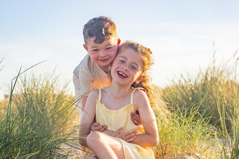 Two children smiling in a sunny outdoor setting.