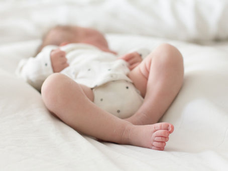 newborn baby sleeping on a white sheet, wearing a cream baby grow with stars