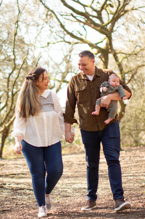 parents walk in the woods holding baby son