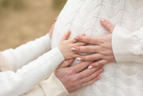 a child holds a woman 's hand on her pregnant belly