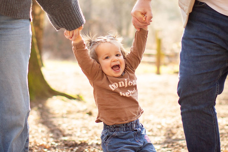 toddler hanging from parents hands in woodland kent