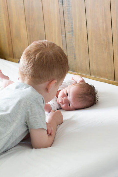a brother and baby sister gazing at each other on a bed