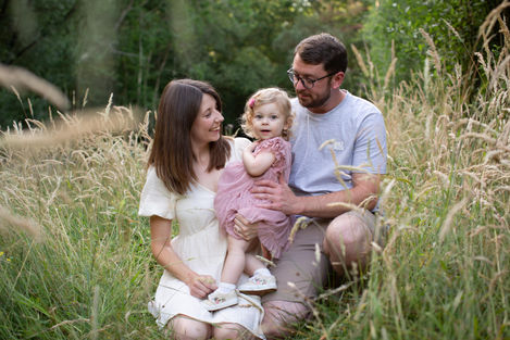family of 3 embrace in meadow