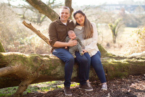 parents sit on log holding baby son