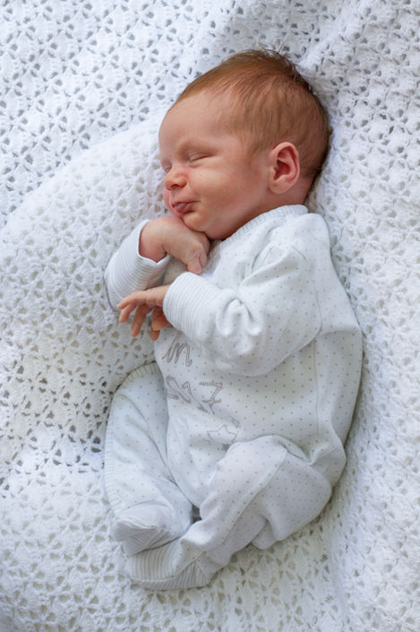 a baby is sleeping on a white blanket and has the letter m on his shirt
