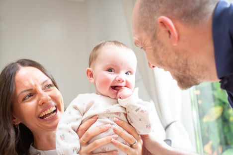 Smiling family with a baby indoors, bright setting.