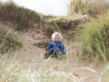 Young girl in blue coat sits on a sand dune during a family photography shoot at the beach