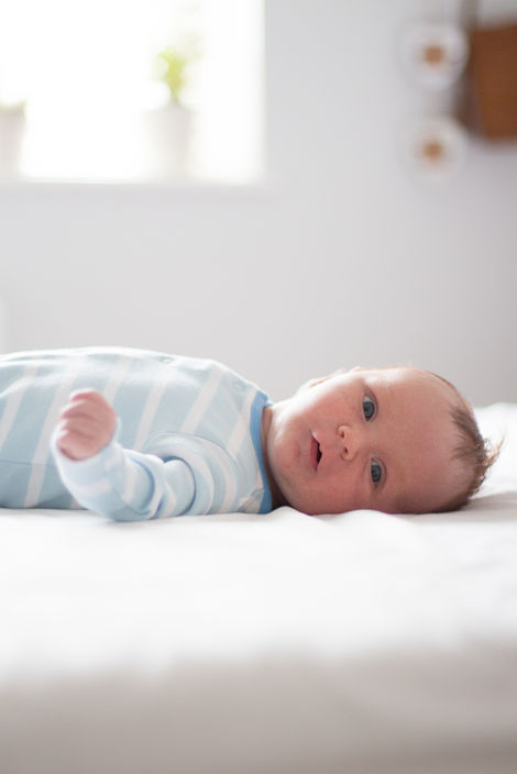 a baby wearing a blue and white striped babygrow is laying on a bed